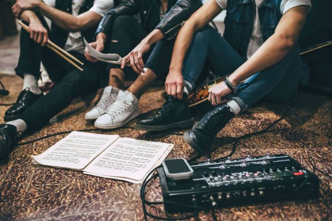 Music band repetition Repetition of rock music band. Cropped image of guitar players and drummer are sitting on the floor at rehearsal base with notes.