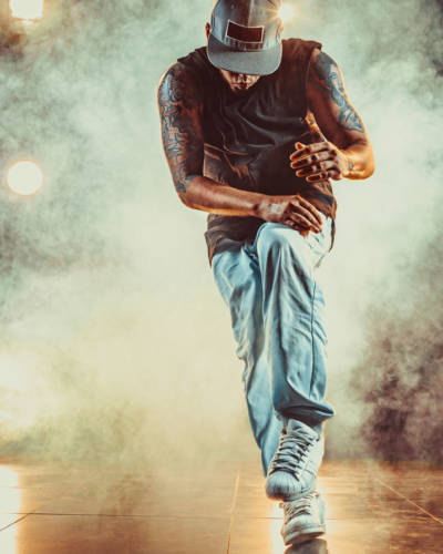 Young cool man break dancing in club with lights and smoke. Tattoo on body.