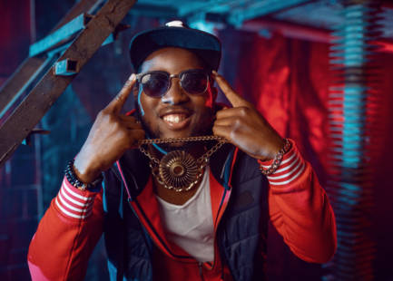Smiling Rapper with gold chain posing in grunge studio with cool underground decoration. Hip-hop performer, rap singer, break-dance performance