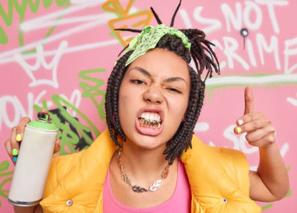 Swag. Fashionable hipster girl rapper with dreadlocks and golden teeth goes out to paint in public places holds spray aerosol creats graffiti on walls being passionate street artist. Young people